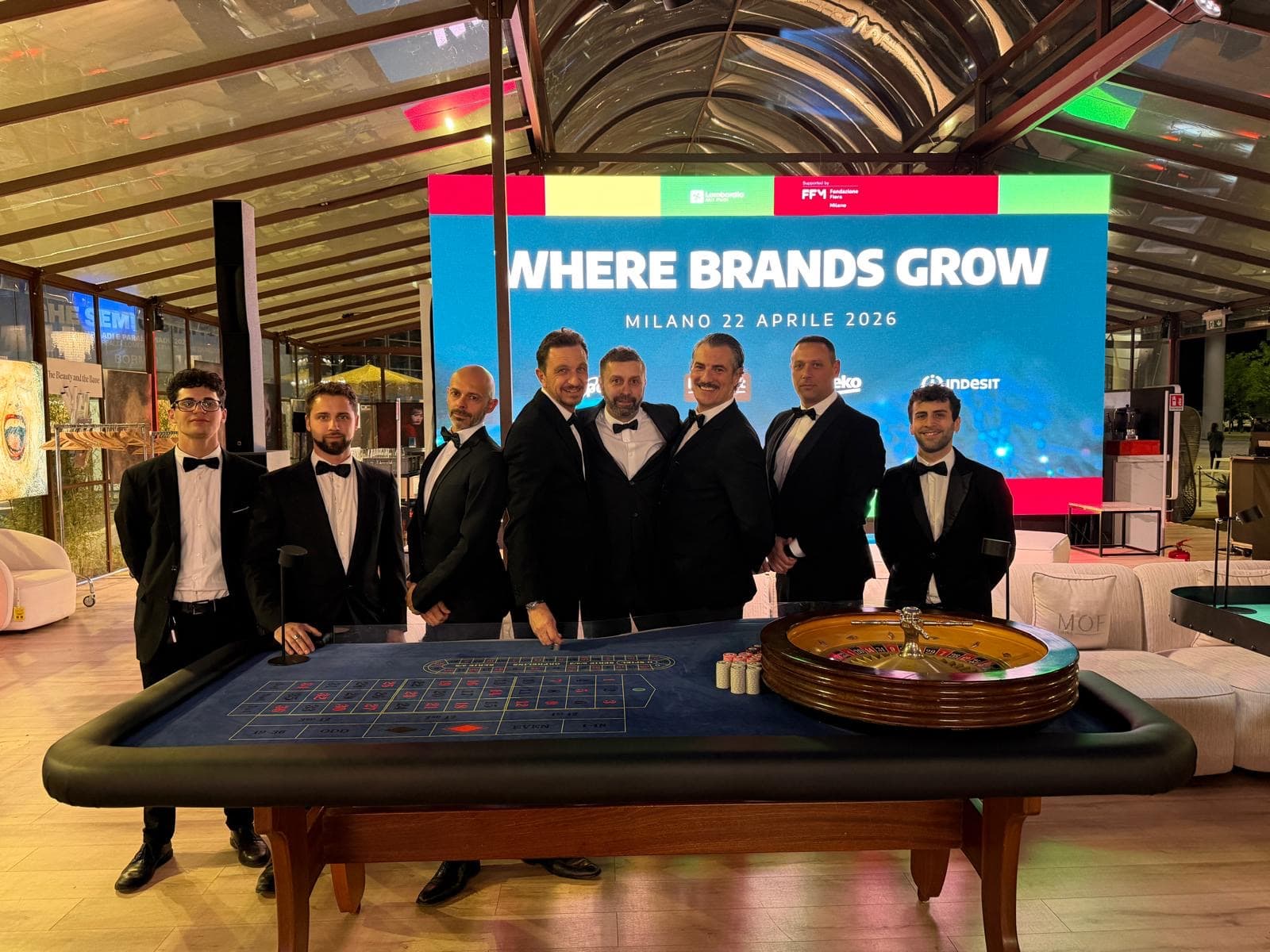 Croupier Fun Casinò in smoking a un tavolo da roulette, in una location con un grande schermo
